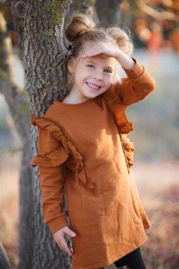 Gün batımında güzel bir sonbahar parkında fotoğrafçı için poz veren tatlı bir kız. Küçük moda tutkunu. Sonbahar yapraklarıyla gülümseyen küçük bir kız. Kızlar sonbahar stili. Küçük kız sonbahar mevsimi için heyecanlı. Sıcak mevsim hoş anlar..