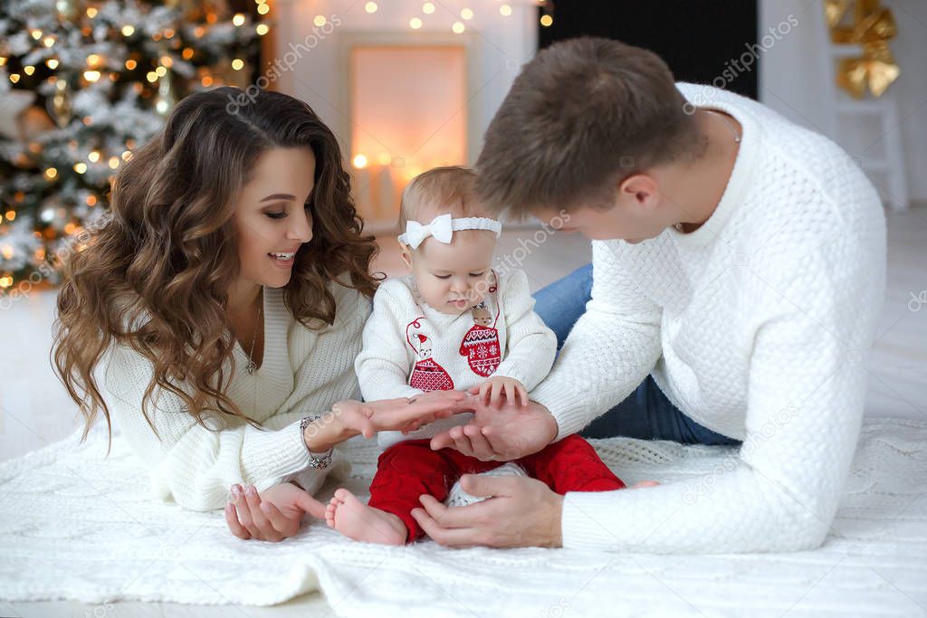A happy family, father, mother and little daughter, spend time together on Christmas evening in a bright room indoors against a background of a beautifully decorated Christmas tree with garlands and golden balls.Merry Christmas with family at home