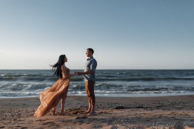 Deniz kenarında şafak vakti aşık bir çift. Balayı gezisi. Erkek ve kadın seyahat ediyor. Deniz manzaralı mutlu bir çift. Erkek ve kadın el ele tutuşuyor. Tatilde aşık bir çift. Beni takip edin. Güneşli bir günde, mavi okyanusun kayalık sahillerinde bir çift