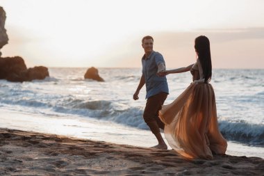 Deniz kenarında şafak vakti aşık bir çift. Balayı gezisi. Erkek ve kadın seyahat ediyor. Deniz manzaralı mutlu bir çift. Erkek ve kadın el ele tutuşuyor. Tatilde aşık bir çift. Beni takip edin. Güneşli bir günde, mavi okyanusun kayalık sahillerinde bir çift