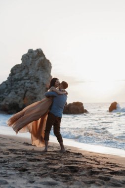Deniz kenarında şafak vakti aşık bir çift. Balayı gezisi. Erkek ve kadın seyahat ediyor. Deniz manzaralı mutlu bir çift. Erkek ve kadın el ele tutuşuyor. Tatilde aşık bir çift. Beni takip edin. Güneşli bir günde, mavi okyanusun kayalık sahillerinde bir çift