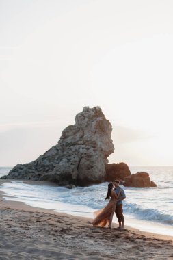 Deniz kenarında şafak vakti aşık bir çift. Balayı gezisi. Erkek ve kadın seyahat ediyor. Deniz manzaralı mutlu bir çift. Erkek ve kadın el ele tutuşuyor. Tatilde aşık bir çift. Beni takip edin. Güneşli bir günde, mavi okyanusun kayalık sahillerinde bir çift