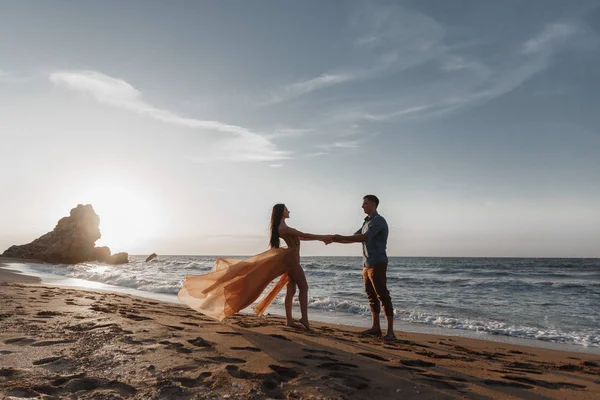 海のそばで夜明けに恋にカップル 新婚旅行だ男性と女性の旅行 背中から海の景色によって幸せなカップル 手を握っている男と女 休暇中のカップル ついて来い晴れた日には青い海の岩のビーチでカップル — ストック写真