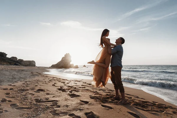 Deniz kenarında şafak vakti aşık bir çift. Balayı gezisi. Erkek ve kadın seyahat ediyor. Deniz manzaralı mutlu bir çift. Erkek ve kadın el ele tutuşuyor. Tatilde aşık bir çift. Beni takip edin. Güneşli bir günde, mavi okyanusun kayalık sahillerinde bir çift