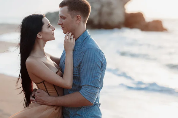 Couple in love at dawn by the sea. Honeymoon trip. Man and woman traveling. Happy couple by the sea view from the back. Man and woman holding hands. Couple in love on vacation. Follow me. Couple on a rocky beach of blue ocean on a sunny day