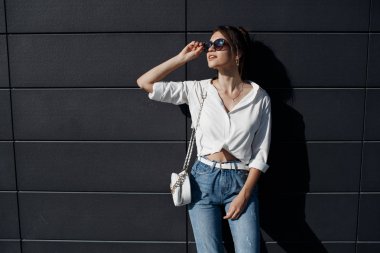 Kot pantolonlu, açık havada poz veren uzun saçlı esmer bir kadın. Moda fotoğrafı konsepti. İş merkezine yakın bir kadın. Esmer bir kadının portresi. Ofisinin yanında güzel bir kadın iş merkezi çalışanı.