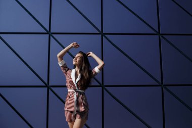 Kot pantolonlu, açık havada poz veren uzun saçlı esmer bir kadın. Moda fotoğrafı konsepti. İş merkezine yakın bir kadın. Esmer bir kadının portresi. Ofisinin yanında güzel bir kadın iş merkezi çalışanı.