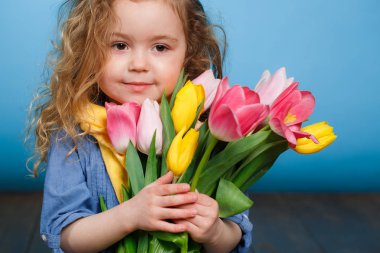 Kırmızı kıvırcık saçlı bir kızın bahar portresi. Stüdyoda açık yeşil bir arka planda duran bir buket çok renkli laleyi hediye olarak tutuyor. Stüdyoda, bir buket lale ile küçük şirin bir kız..