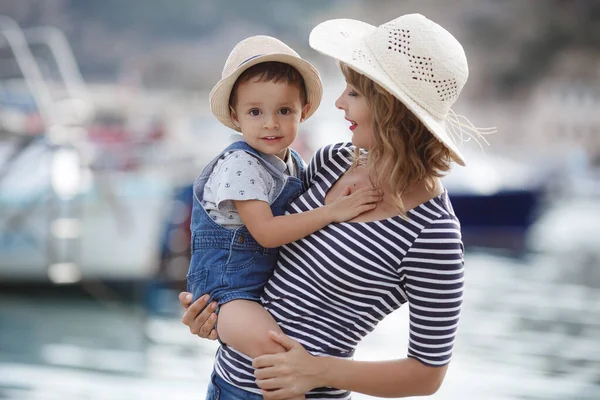 母親と小さな息子は一緒に夏に屋外で時間を過ごします ボートやボートの近くの桟橋に座って 若い母親は 遊歩道で彼女の赤ちゃんと遊ぶ リゾートの母親と息子は — ストック写真