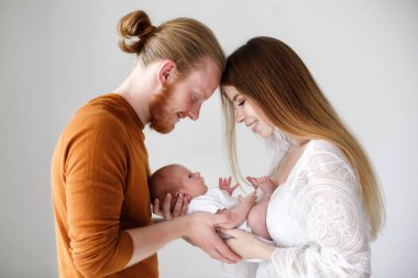 Ebeveynlik, sevgi ve aile kavramı - gülümseyen anne ve baba, bebeğini kucağına alıyor. Mutlu Avrupalı aile, baba ve oğul. Stüdyoda yeni doğmuş bir oğlu olan genç ebeveynler beyaz bir altyapıya sahipler..