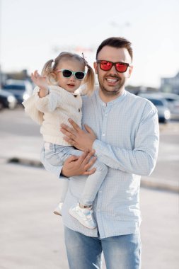 Beyaz bir baba, küçük kızıyla marketten alışveriş yapıyor. Babam taze sebze alıyor. Küçük kızı olan mutlu bir baba otoparkta elinde taze sebzeler ve alışveriş torbalarıyla yürüyor..