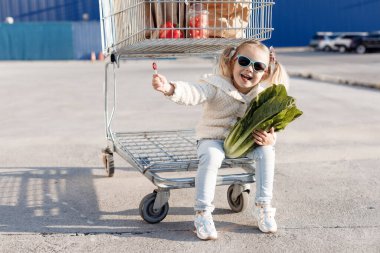 Üç yaşında bir kız markette ya da süpermarkette taze organik lahana seçiyor. Çocuklu genç bir aile için sağlıklı yiyecekler. Küçük bir alıcının elinde taze yeşil Pekin lahanası. Sokakta lahana kafalı bir çocuk..