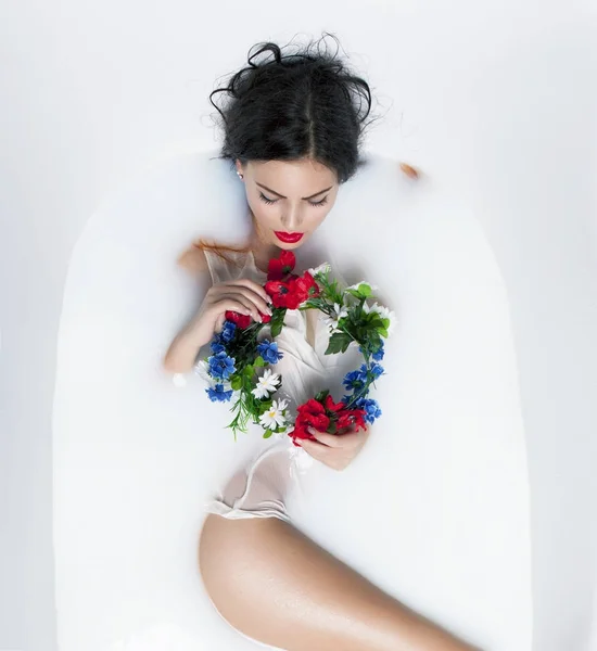 Sexy brunette model in milk bath with the crown from flowers — Stock Photo, Image