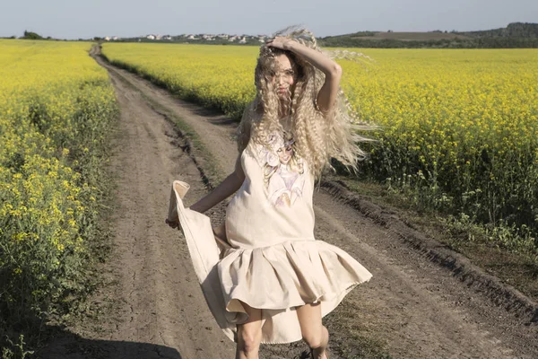 Winderige zomerdag en een blij meisje lopend op de achtergrond van een veld. — Stockfoto