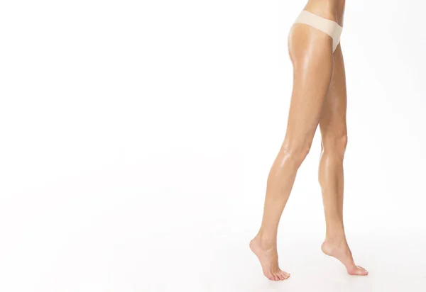 Сексуальные загорелые ноги девушки и бежевые стринги, студия снята на белом Стоковая Картинка