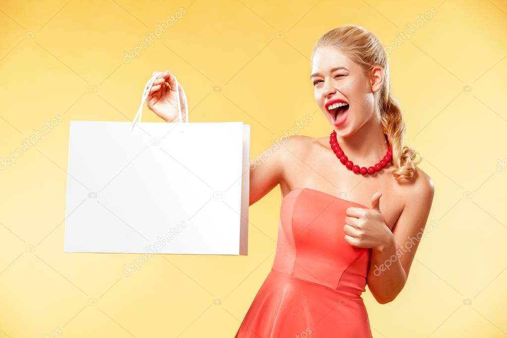Shopping. Young smiling woman showing sale bag make her thumb up in black friday holiday. Girl on yellow background with copy space