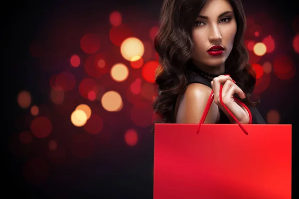 Mulher de compras segurando saco vermelho no fundo de Natal com luzes bokeh no feriado de sexta-feira preta — Fotografia de Stock