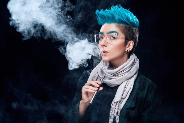 Hipster donna con capelli blu fumo vaporizzatore su sfondo nero — Foto Stock