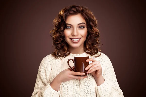 Bela jovem com uma xícara de café em pé sobre o fundo marrom — Fotografia de Stock