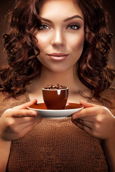 Όμορφη νεαρή γυναίκα με ένα φλιτζάνι καφέ στέκεται στο καφέ φόντο — Φωτογραφία Αρχείου