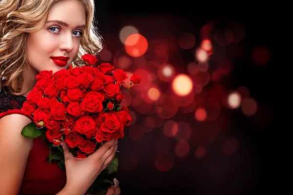 Beautiful blonde woman holding bouquet of red roses on bokeh background. Saint Valentine and International Womens Day, Eight March celebration. Copy space. — Stock Photo, Image