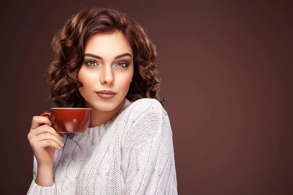 Mooie lachende vrouw met een kopje thee op de bruine achtergrond. Koffie advertentie, kopie ruimte. — Stockfoto