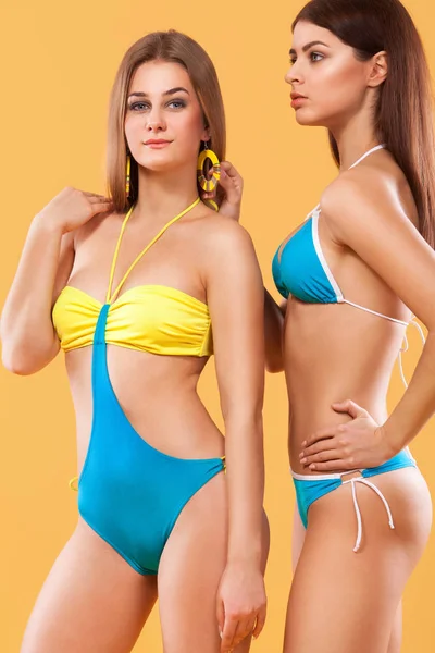 Две сексуальные женщины в купальниках позируют на оранжевом фоне. Идеальное тело. Концепция летней рекламы в Бикини . — стоковое фото