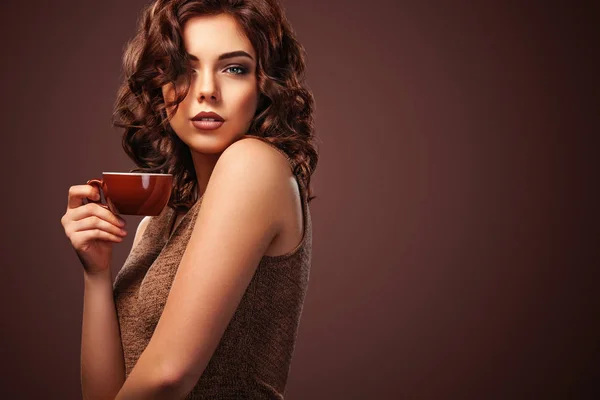 Красивая улыбающаяся женщина с чашкой чая на коричневом фоне. Реклама кофе, место для копирования . — стоковое фото
