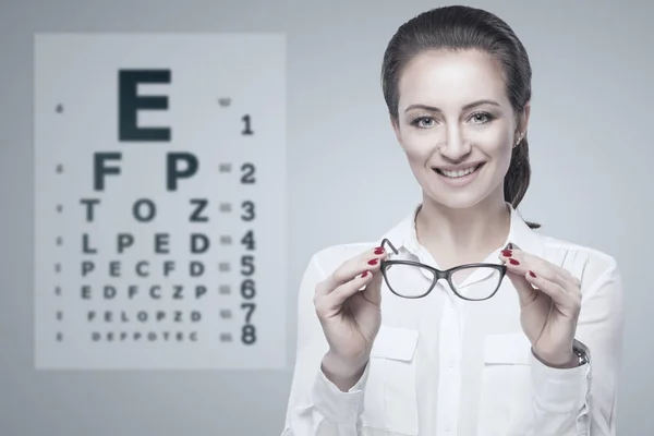 Mujer sosteniendo gafas en las manos con Snellen carta de prueba en el fondo . —  Fotos de Stock