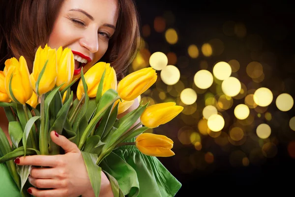 Closeup girl portrait. Beautiful brunette woman smiling with tulip flowers in hands on black background with bokeh lights. — Stock Photo, Image