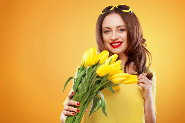 Beautiful young brunette woman with yellow tulips on yellow background — Stock Photo, Image