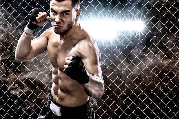 Sportsman muay thai boxer fighting in boxing cage. Background with lights and smoke. Copy Space. Sport concept.