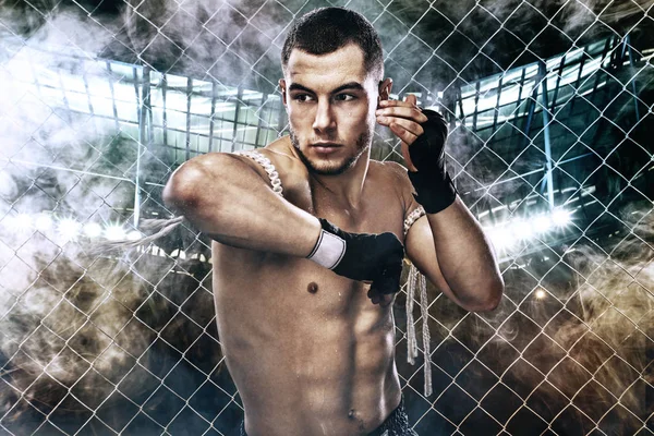 Sportsman Muay Thai Boxer a lutar numa jaula de boxe. Fundo com luzes e fumaça. Espaço de cópia . — Fotografia de Stock