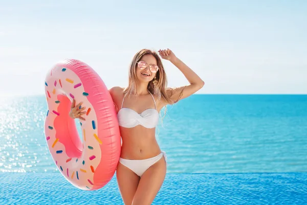 Vacanze estive. Godendo abbronzatura donna in bikini bianco con materasso ciambella vicino alla piscina . — Foto Stock
