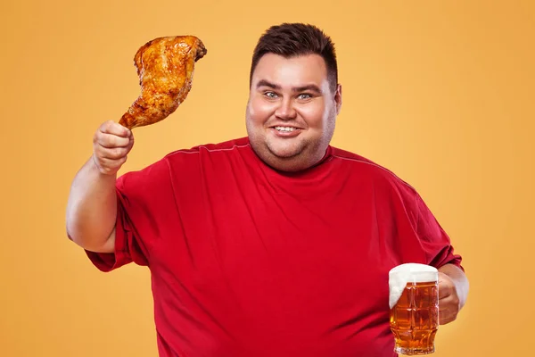 Não desportivo homem gordo no oktoberfest, beber cerveja e comer perna de frango no fundo amarelo . — Fotografia de Stock