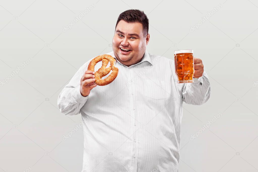 Young fat man at oktoberfest, drinking beer and eating pretzel isolated on white background.
