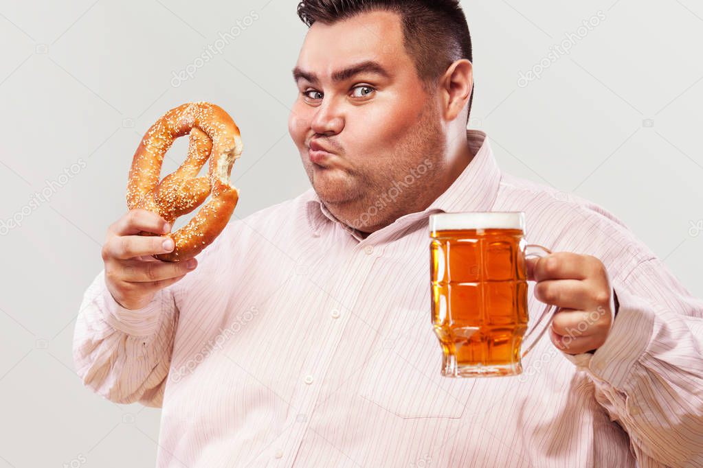 Young fat man at oktoberfest, drinking beer and eating pretzel isolated on white background.