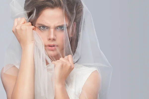 Angry bride with fashion wedding hairstyle - on gray background. Closeup portrait of young gorgeous bride. Wedding. Studio shot with copy space. Beautiful bride portrait with veil over her face — Stock Photo, Image
