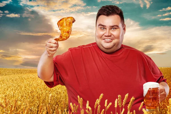 Not sporty fat man at oktoberfest, drinking beer and eating chicken leg on yellow background. — Stock Photo, Image