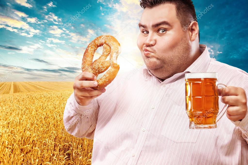Young fat man at oktoberfest, drinking beer and eating pretzel on yellow background.