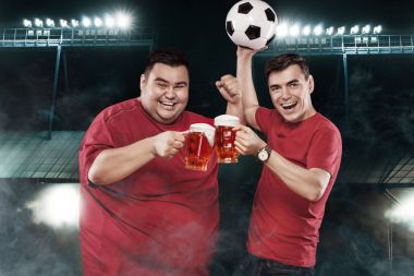 İki futbol eğlenceler - bira ve futbol topu koyu arka plan üzerine alarak spor stadyumunda futbol izlerken mutlu ve şişman bir adam.