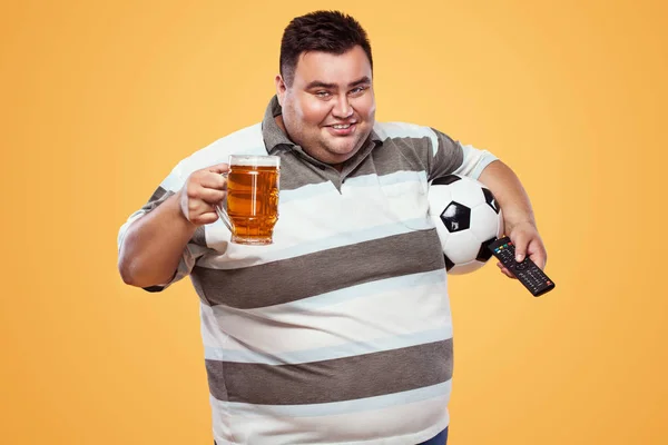 Diversión de fútbol - hombre feliz y gordo en oktoberfest, tomando cerveza y pelota de fútbol sobre fondo amarillo . — Foto de Stock