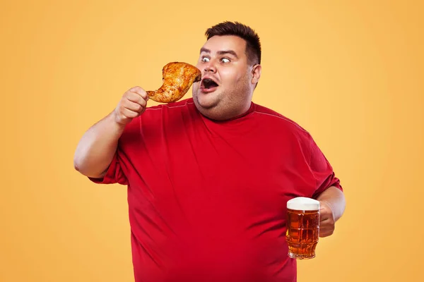不运动的胖男人在慕尼黑啤酒节，喝啤酒和吃鸡腿在黄色背景上. — 图库照片