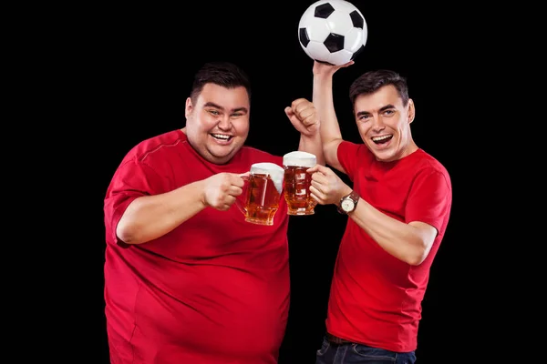 Два футбольных фаната - счастливые мужчины смотрят спорт по телевизору, берут пиво и футбольный мяч на черном фоне . — стоковое фото