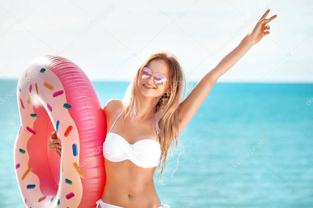 Summer Vacation. Enjoying suntan woman in white bikini with donut mattress near the ocean.