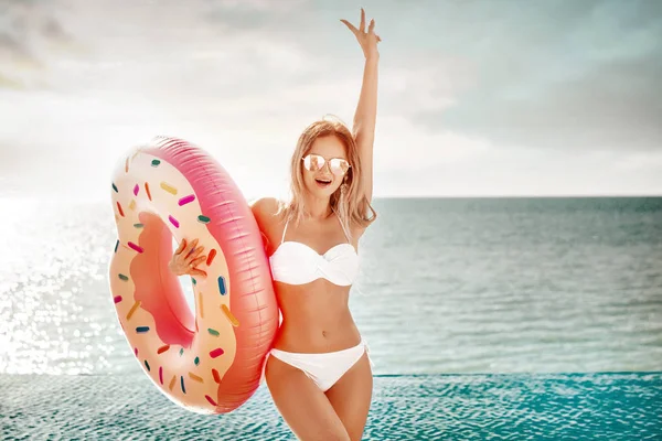 Vacaciones de verano. Disfrutando de una mujer bronceadora en bikini blanco con colchón de rosquillas cerca del océano . — Foto de Stock