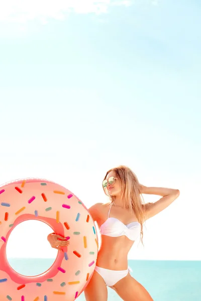 Vacanze estive. Godendo abbronzatura donna in bikini bianco con materasso ciambella vicino al mare . — Foto Stock