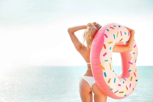 Sommerferien. Sonnenbräune Frau im weißen Bikini mit Donut-Matratze am Meer. — Stockfoto