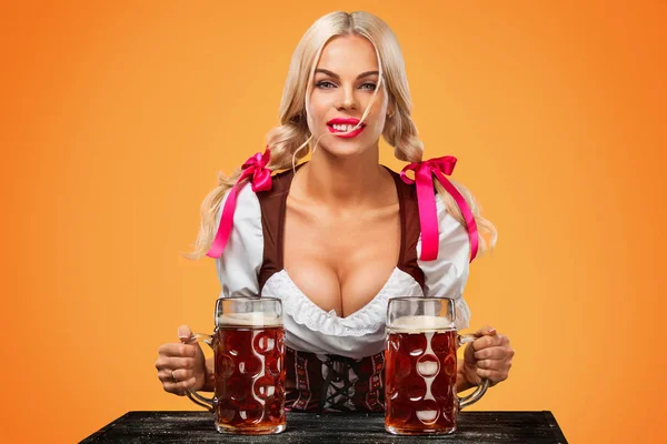 Νεαρό κορίτσι Oktoberfest σέξι - σερβιτόρα, φοράει ένα παραδοσιακό φόρεμα το βαυαρικό, εξυπηρετώντας μεγάλο μπύρα κούπες σε πορτοκαλί φόντο. — Φωτογραφία Αρχείου
