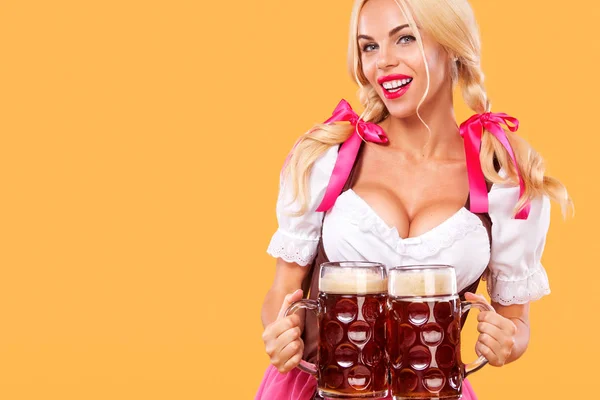 Mladá sexy Oktoberfest dívka - servírka, na sobě tradiční bavorské šaty, slouží velký pivní korbele na pozadí. — Stock fotografie